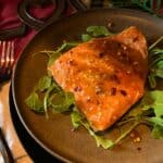 Grilled salmon on cedar plank with maple dijon glaze on a brown plate.