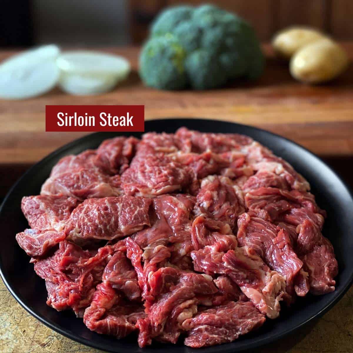 Cut up sirloin meat on a black plate.