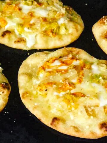 Zucchini blossoms on naan bread with sliced onions, garlic, mozzarella and parmesan cheese.