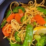 Pancit with vegetables in a black bowl.