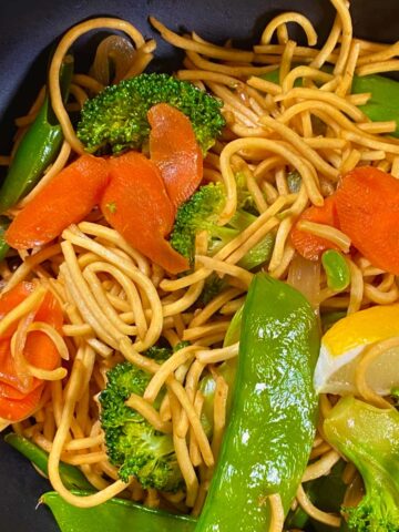 Pancit with vegetables in a black bowl.