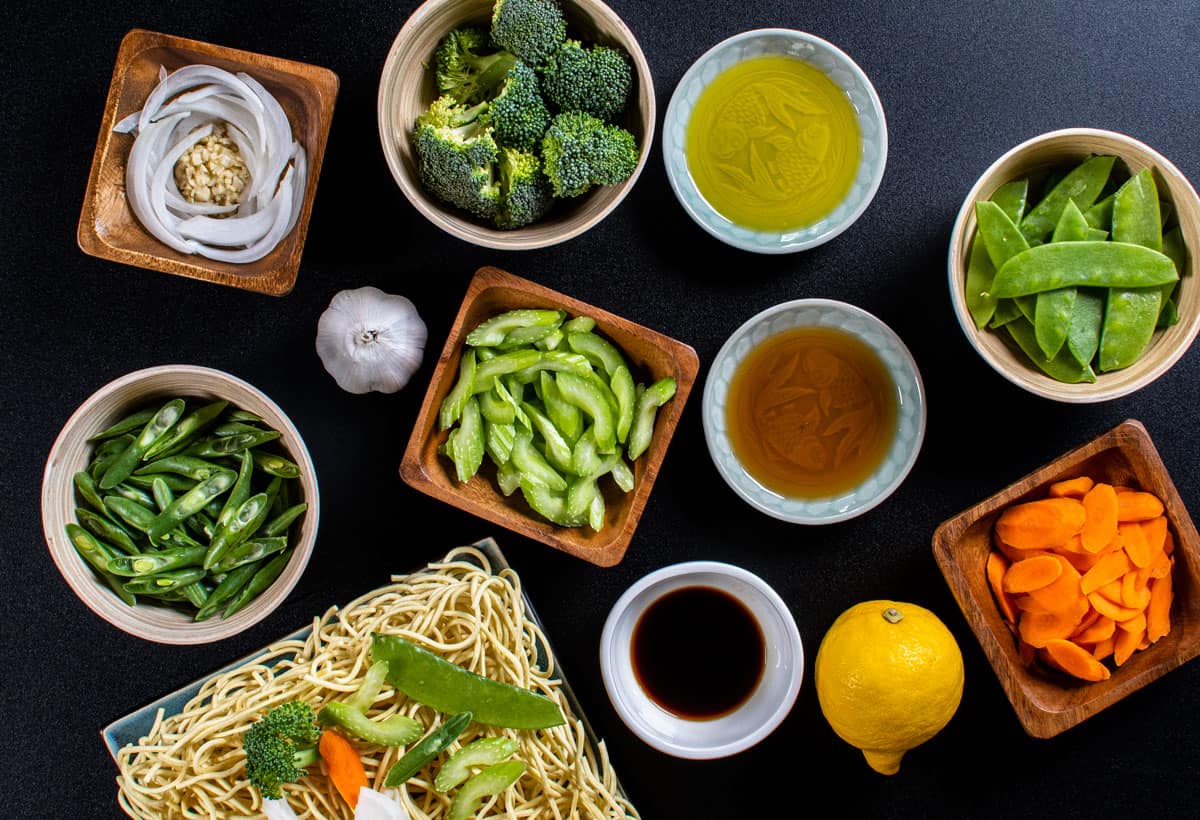 Filipino Vegetable Pancit Noodle ingredients with green beans, garlic, onions, brocolli, celery, pea pods, carrots, lemon, soy sauce, oyster sauce, sesame oil, olive oil