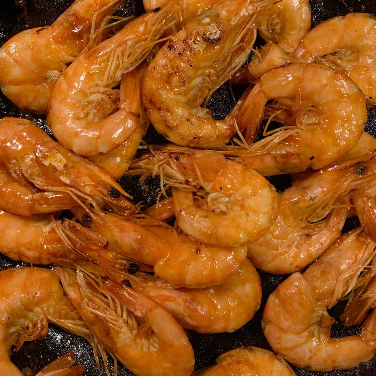 Caramelized Shrimps on a black plate.