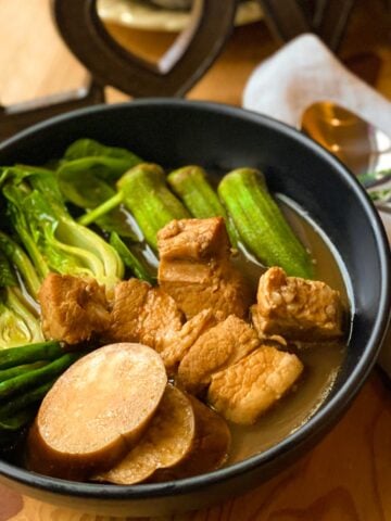 Pork sinigang sour soup with vegetables in a black bowl.