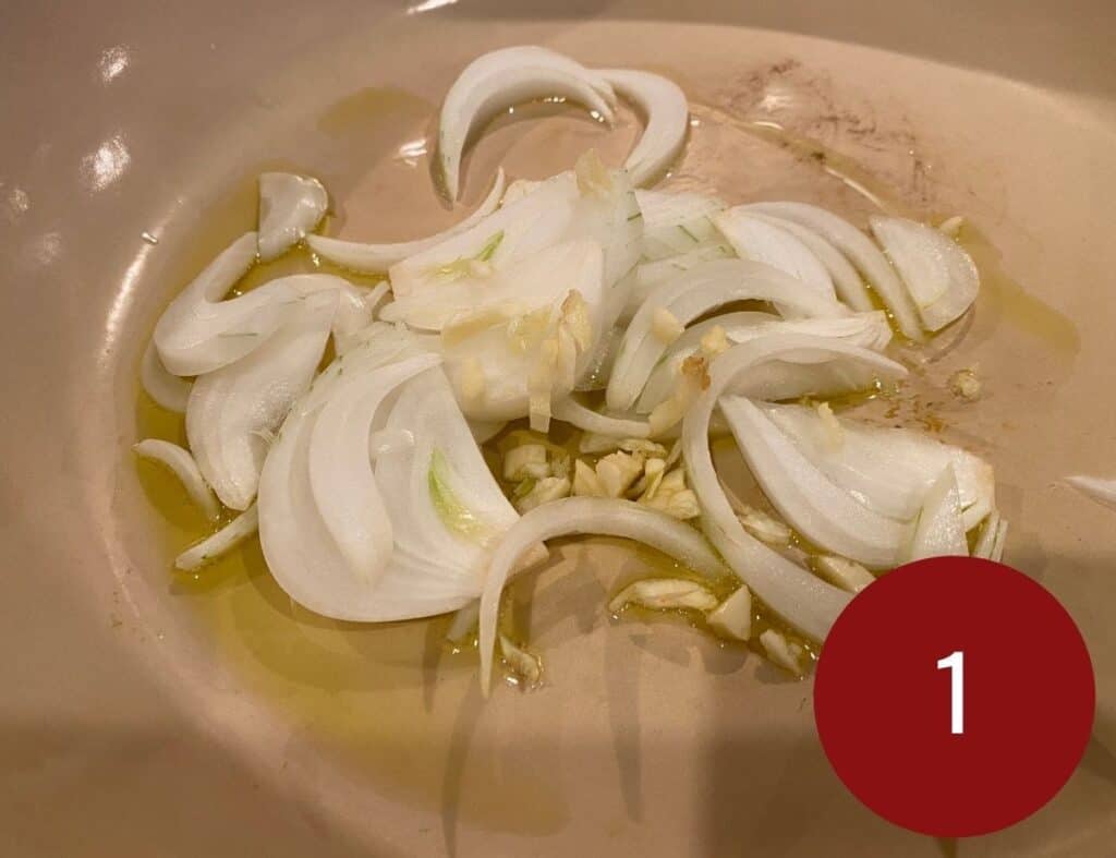 Sliced garlic, onion, ginger in a skillet with olive oil.