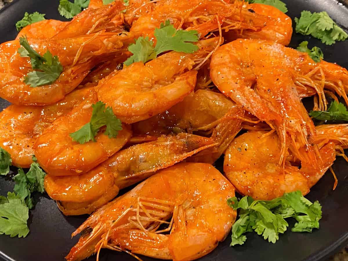 Garlic butter shrimps with cilantro on a black plate.