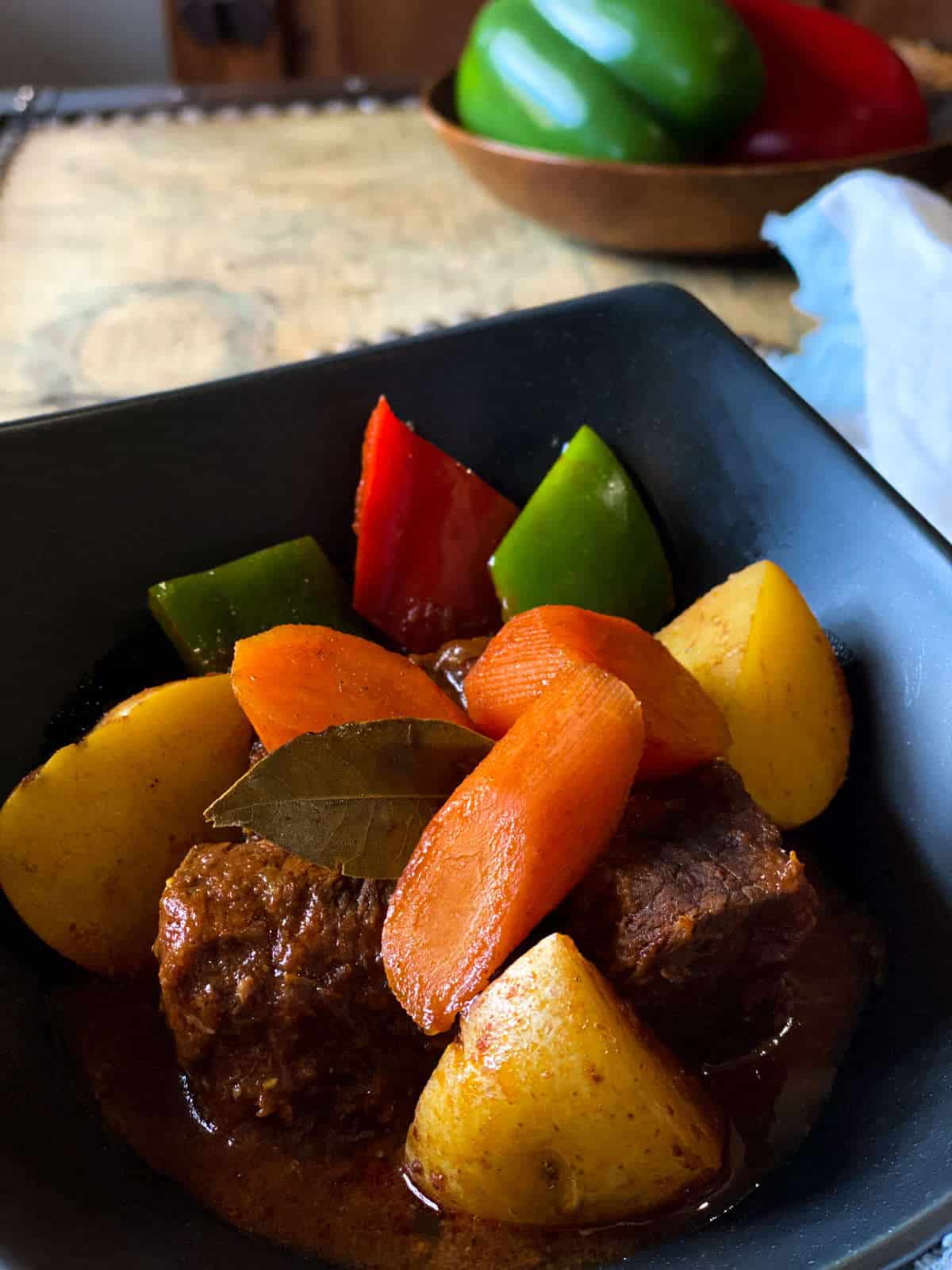 Beef with carrots, potatoes, and red and green bell peppers in a black dish.