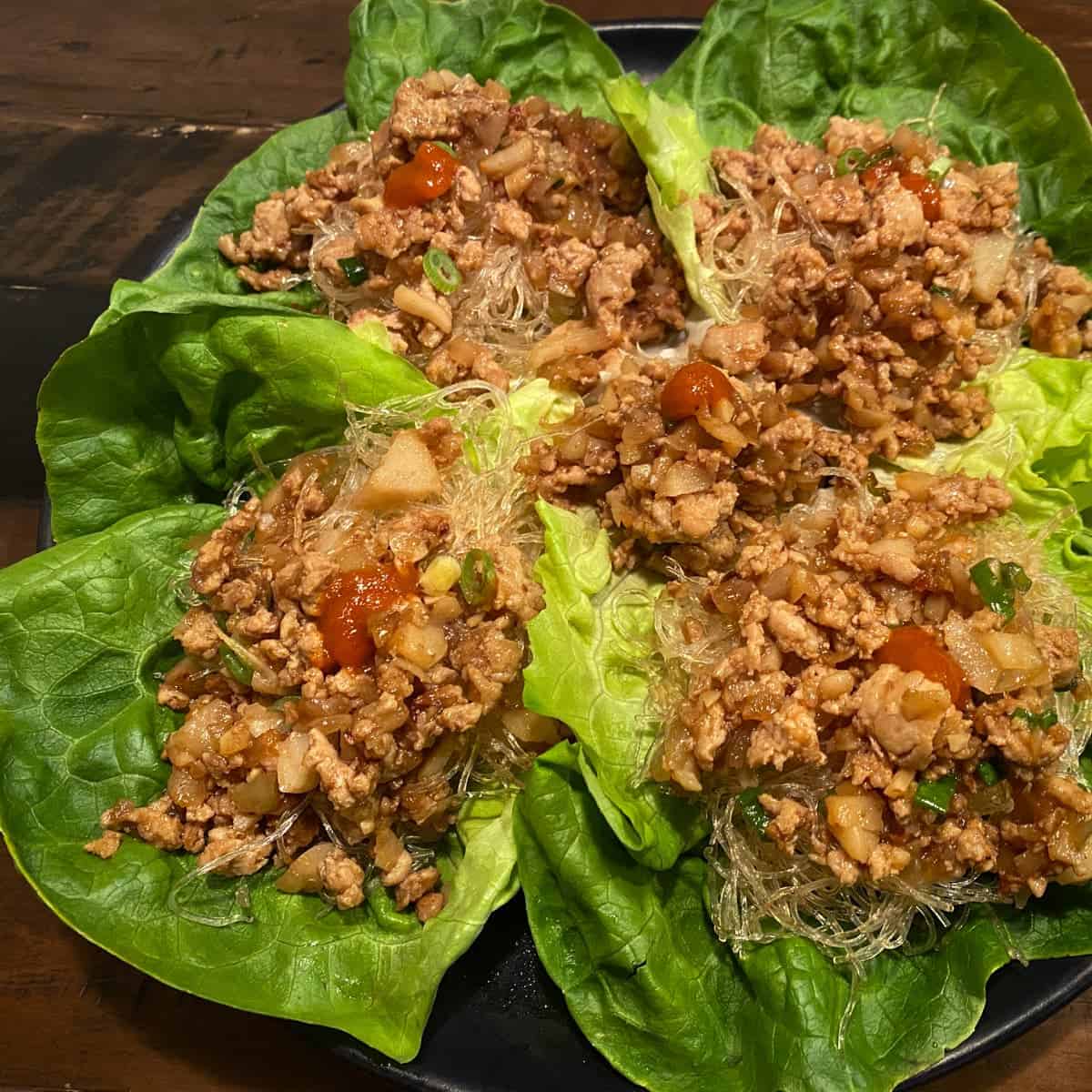 Chicken lettuce wraps on a black plate featured.