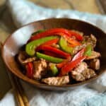 Sliced beef with red and green bell peppers on a wooden bowl with chopsticks on the side.