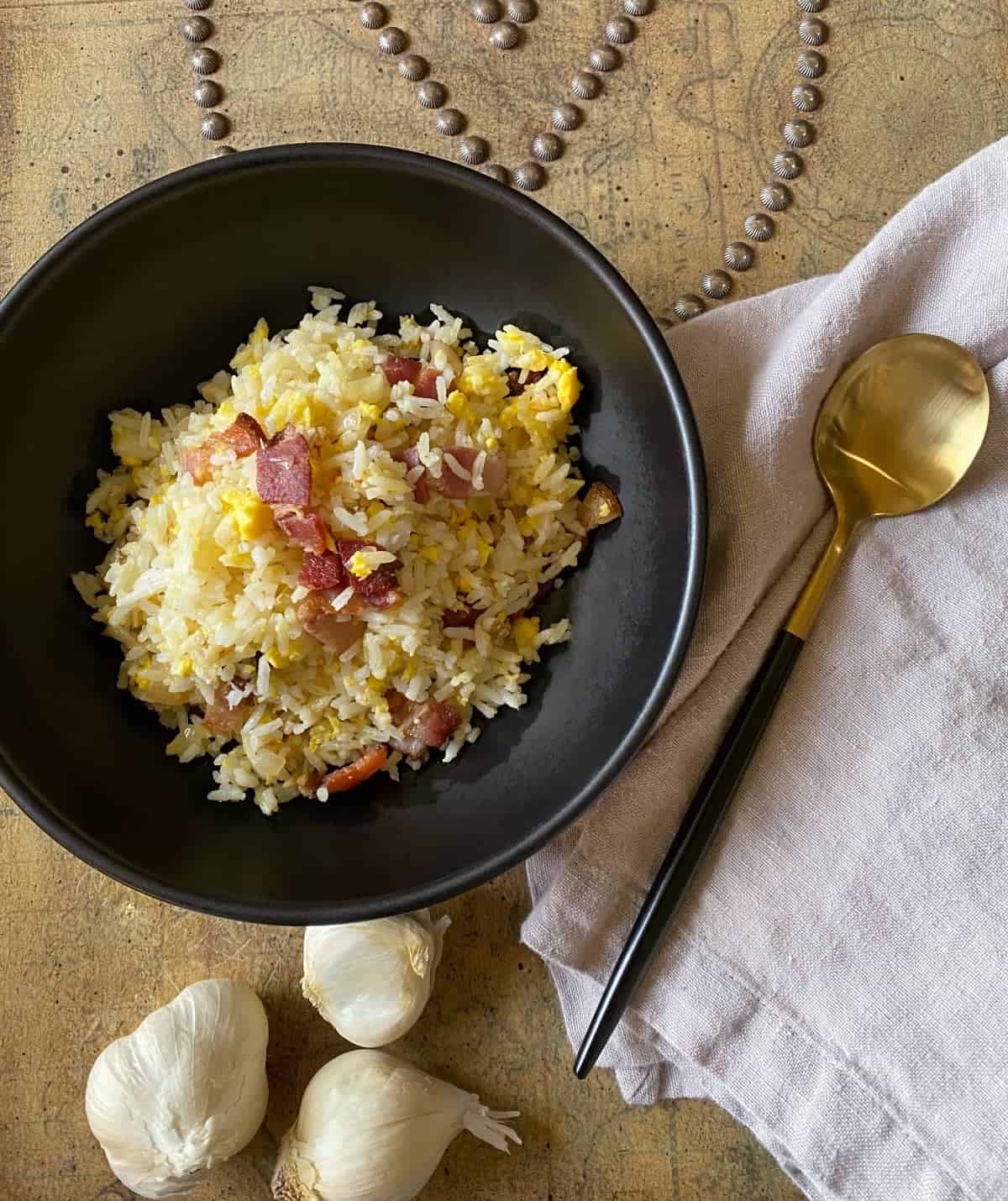 Fried rice with bacon and egg in a black bowl with a spoon on the side.