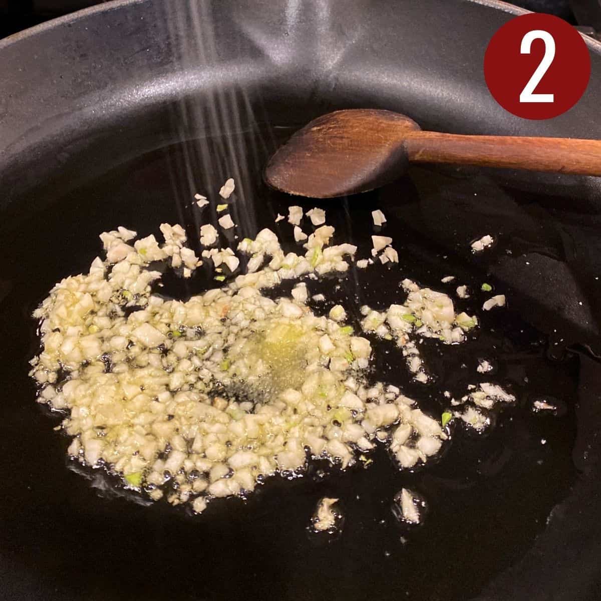 Salt added with garlic in a black skillet.