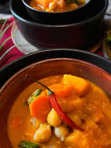 Butternut squash and chickpea curry in a bowl with a red chili pepper on top.