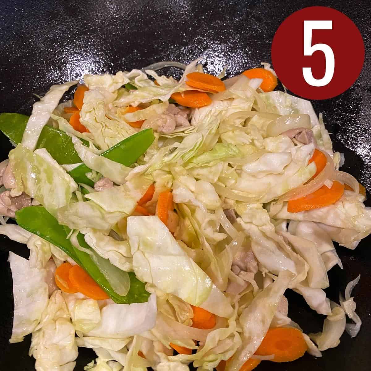 Cabbage, pea pods, carrots with chicken, garlic, and onion with oil in a skillet.
