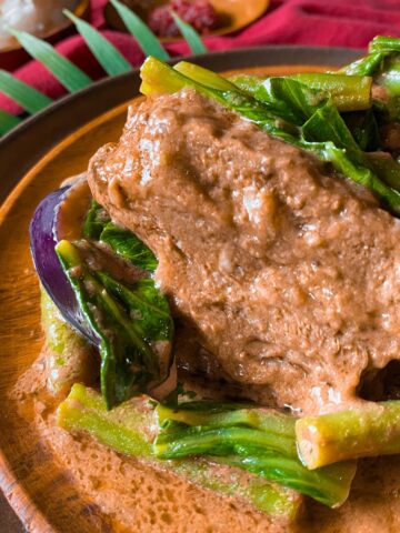 Beef Kare Kare with vegetables on a wooden plate.