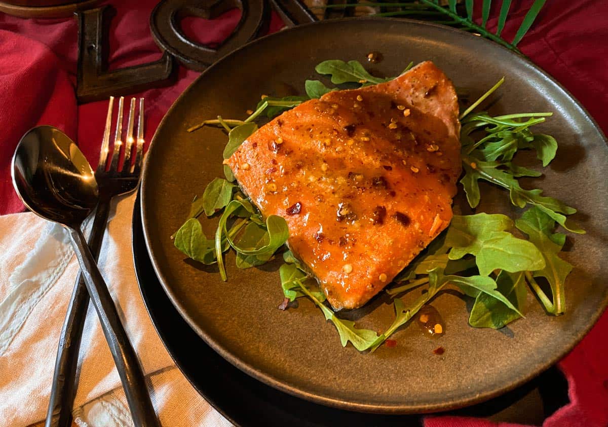 Grilled Salmon with maple dijon glaze and arugula on a brown plate with a spoon and fork on the side.