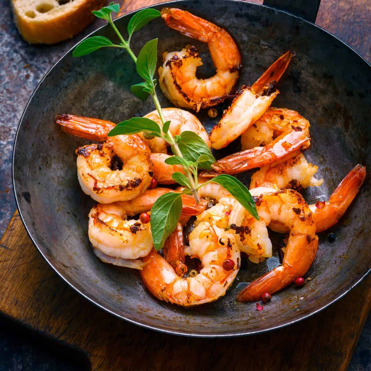 Cooked shrimp with fresh herb in a dark bowl.