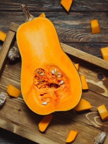 Sliced butternut squash with seed on a wooden tray.