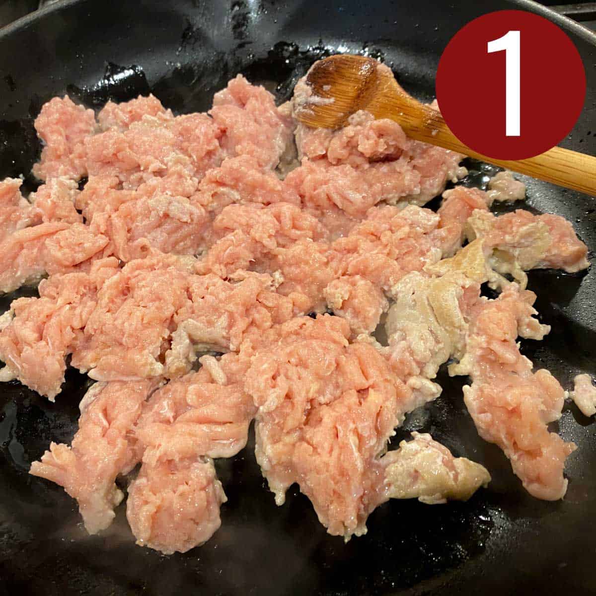 Ground chicken in a skillet with a wooden spoon.