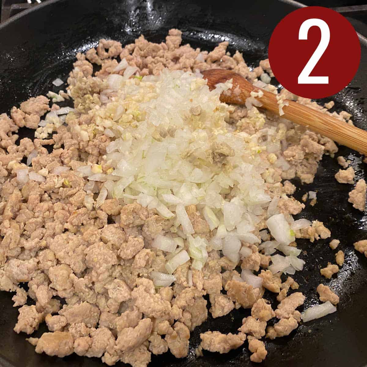 Ground chicken with garlic, onion, and ginger in a skillet.