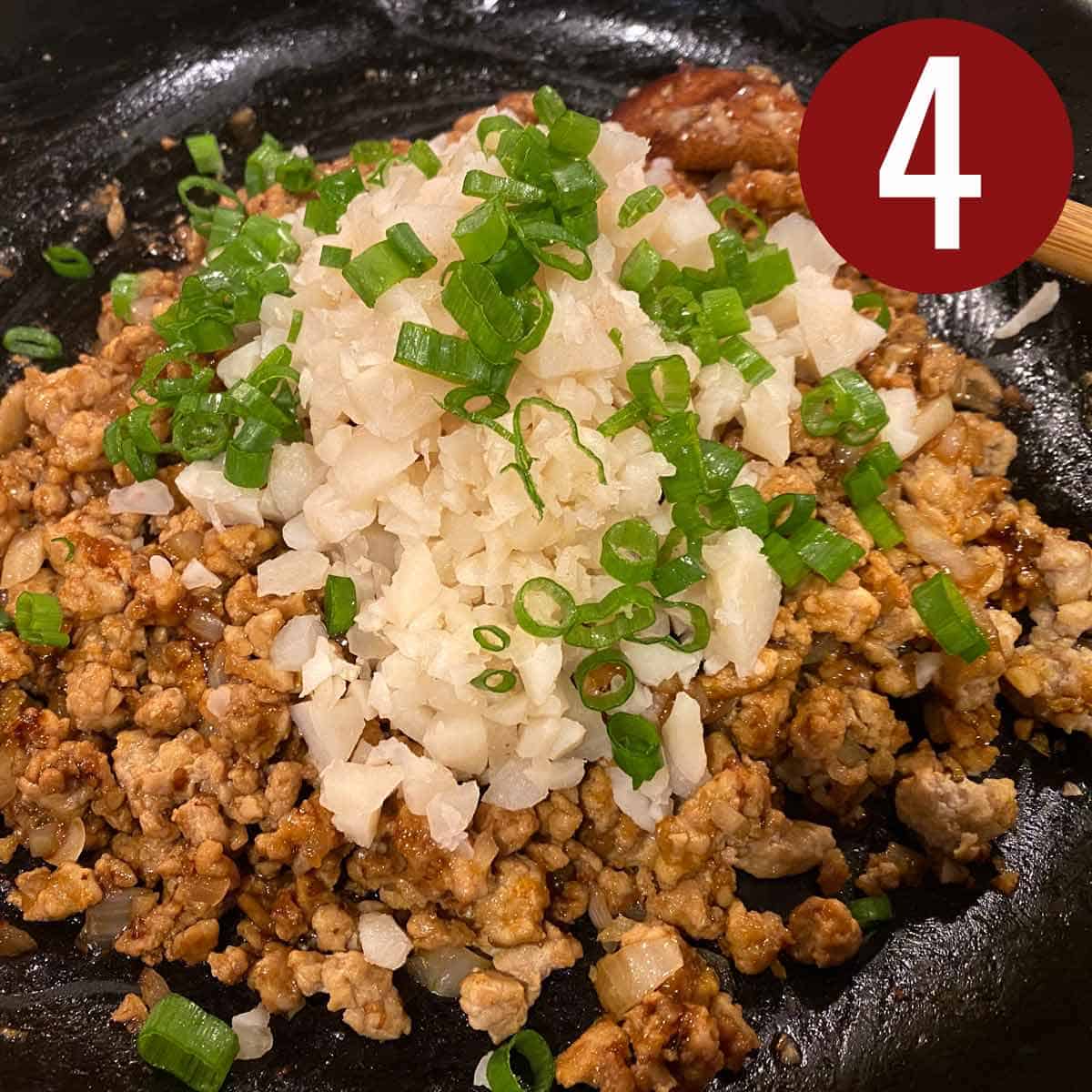 Ground chicken with water chestnuts and sliced gree onions on a black skillet.