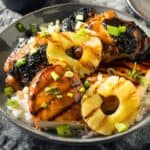 Huli huli chicken with pineapple rings and green onion slices on top of rice in a bowl.