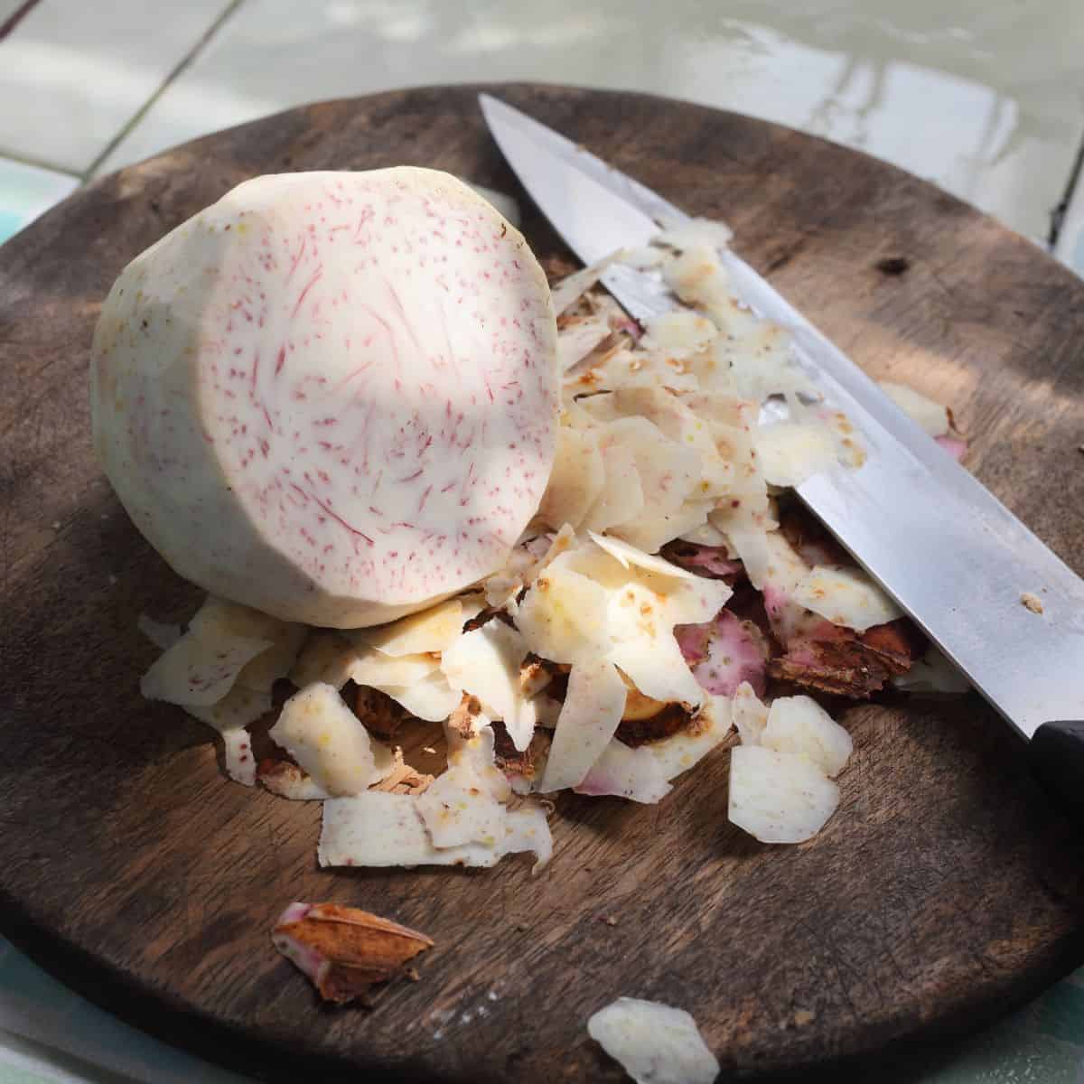 Peeled taro root on a wooden cutting board with a knife.