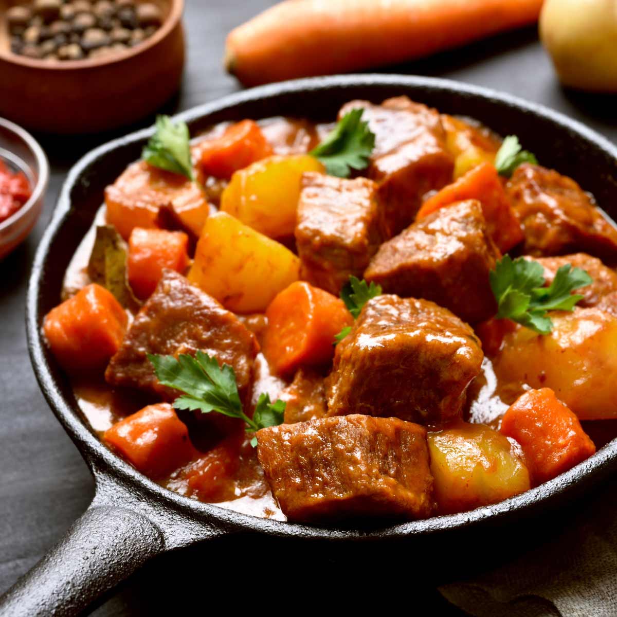 Beef mechado with potatoes and carrots in a black skillet.
