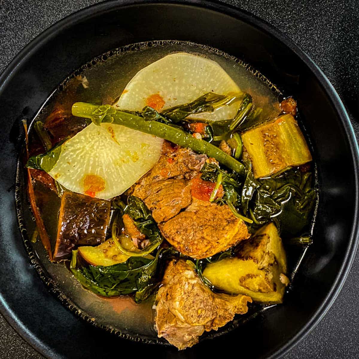 Pork Sinigang with vegetables in a black bowl.