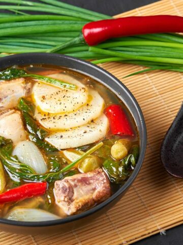Pork ribs sinigang with vegetables in a black bowl.