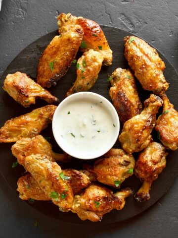 Chicken wings on a black plate with white sauce.