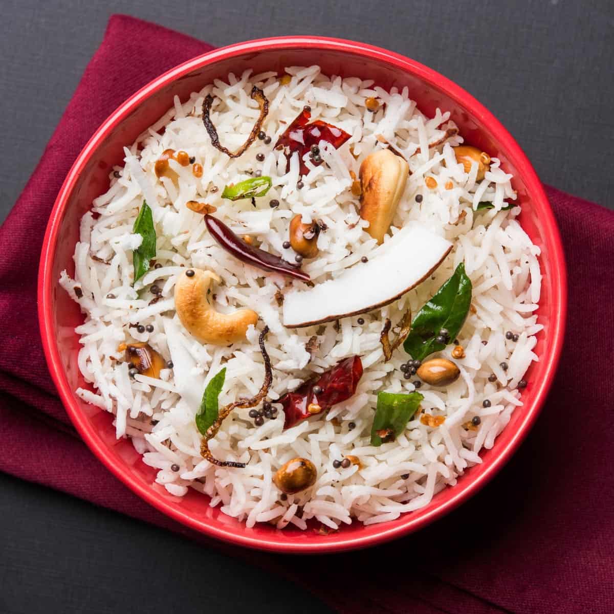 Coconut rice with cashew, herbs, and spices in a red bowl.