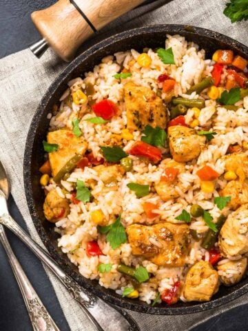 Chicken fried rice with vegetables in a black bowl.