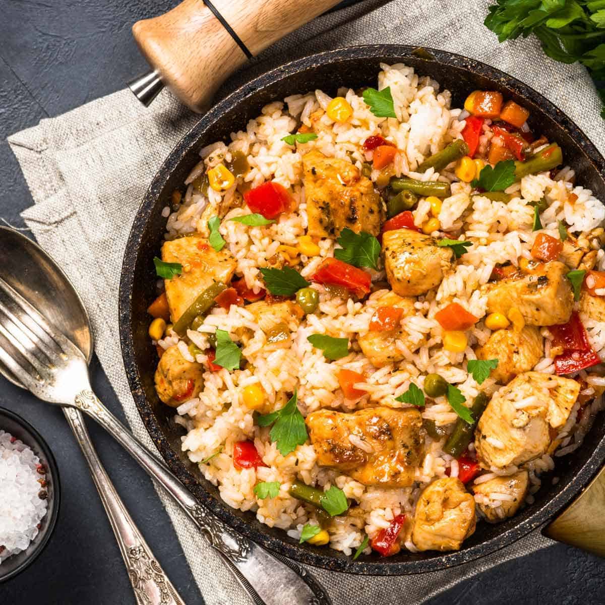 Chicken fried rice with vegetables in a black bowl.