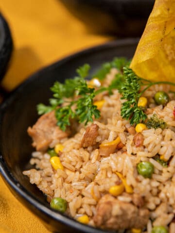 Pork fried rice with peas and corn in a black bowl.