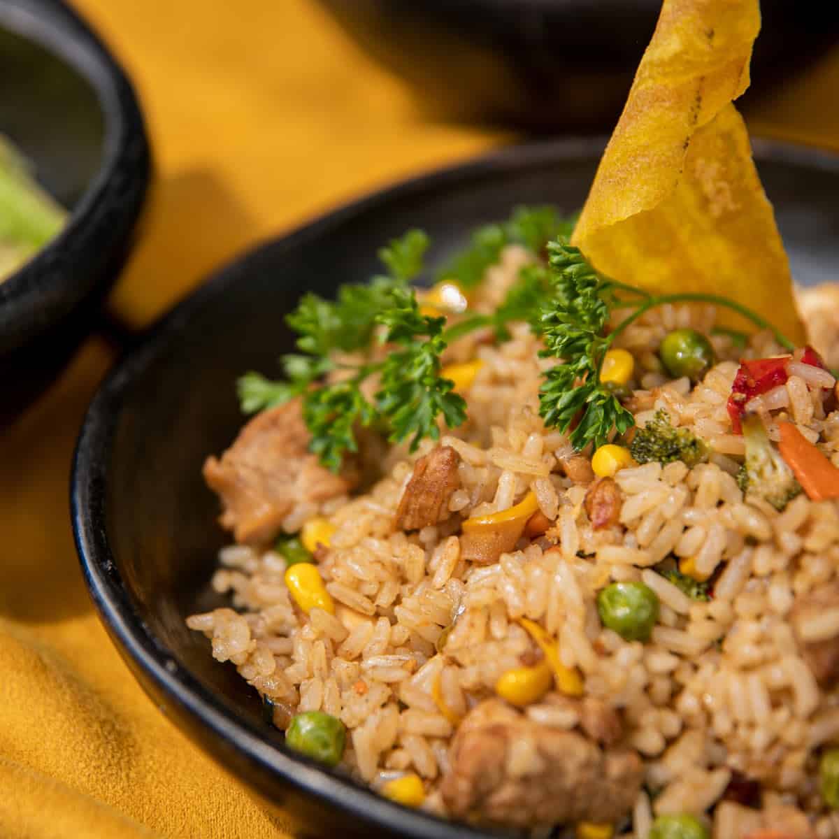 Pork fried rice with peas and corn in a black bowl.
