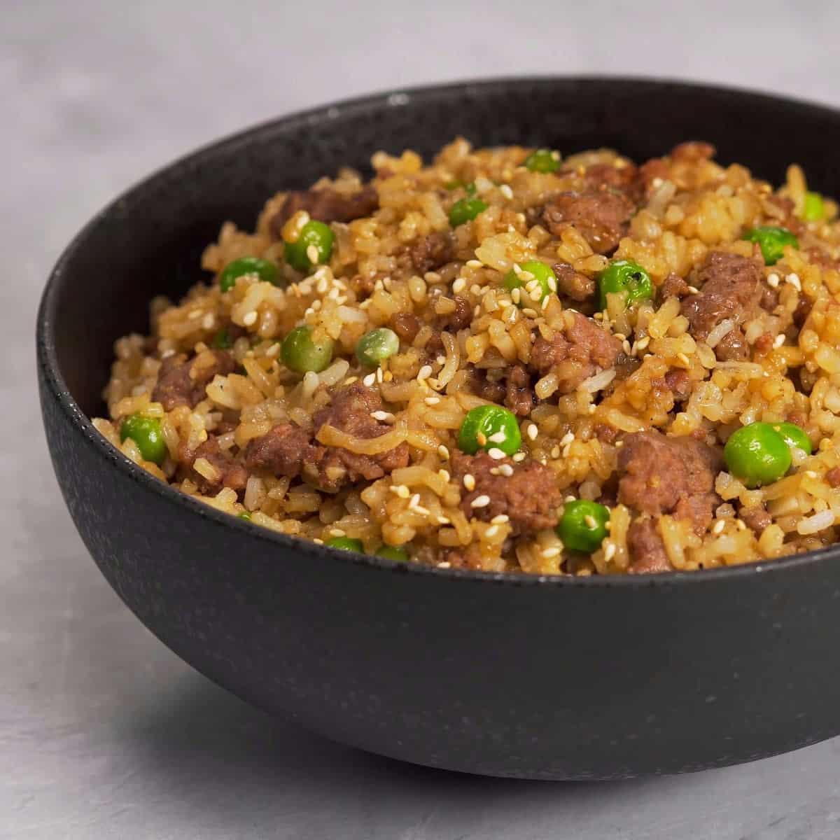 Pork fried rice with peas in a black bowl.
