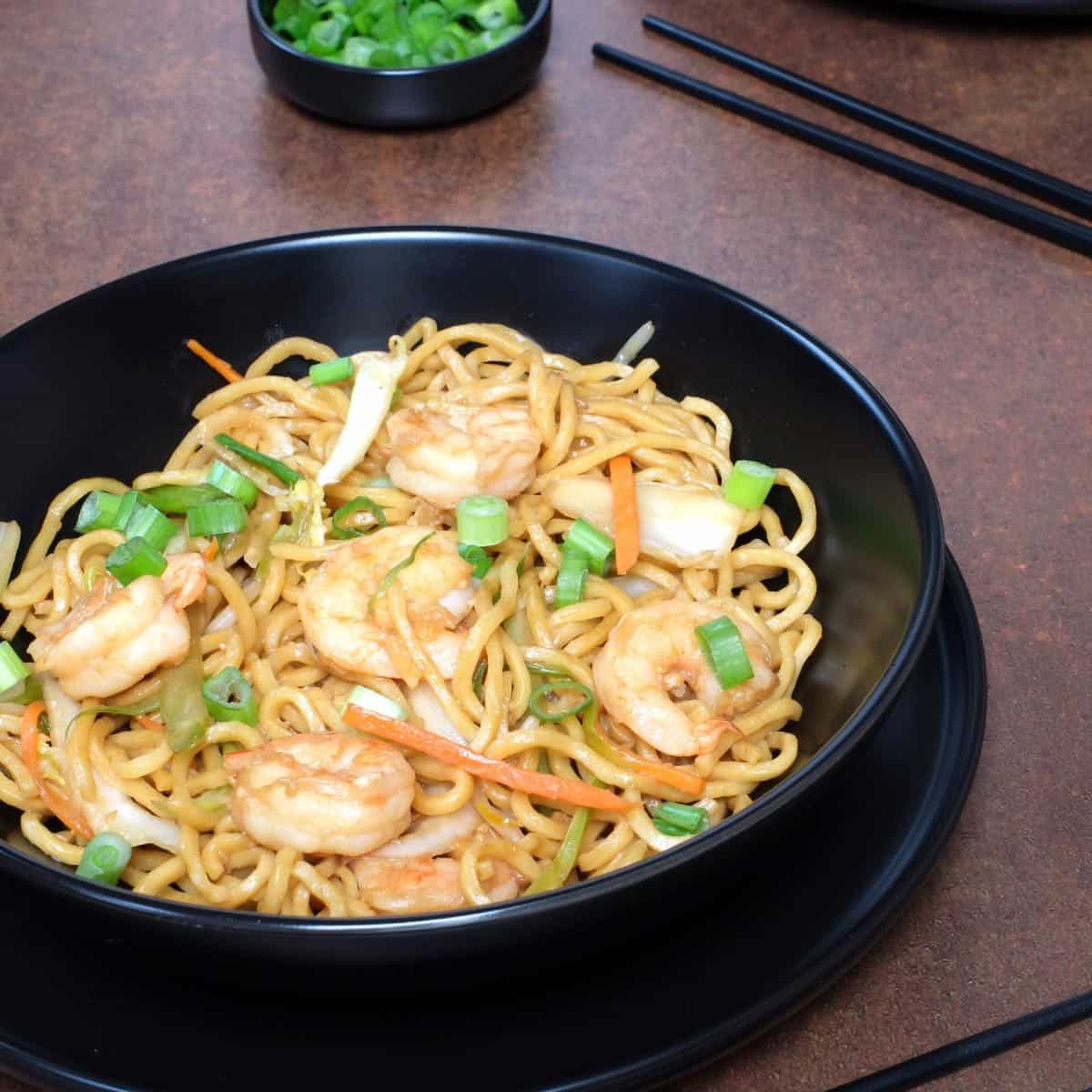 Shrimp Lo Mein with carrots and green onions in a black bowl.
