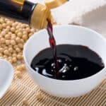 Soy sauce in a white bowl on top of a bamboo mat.