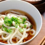 Udon noodle soup with sliced green onion in a white bowl.