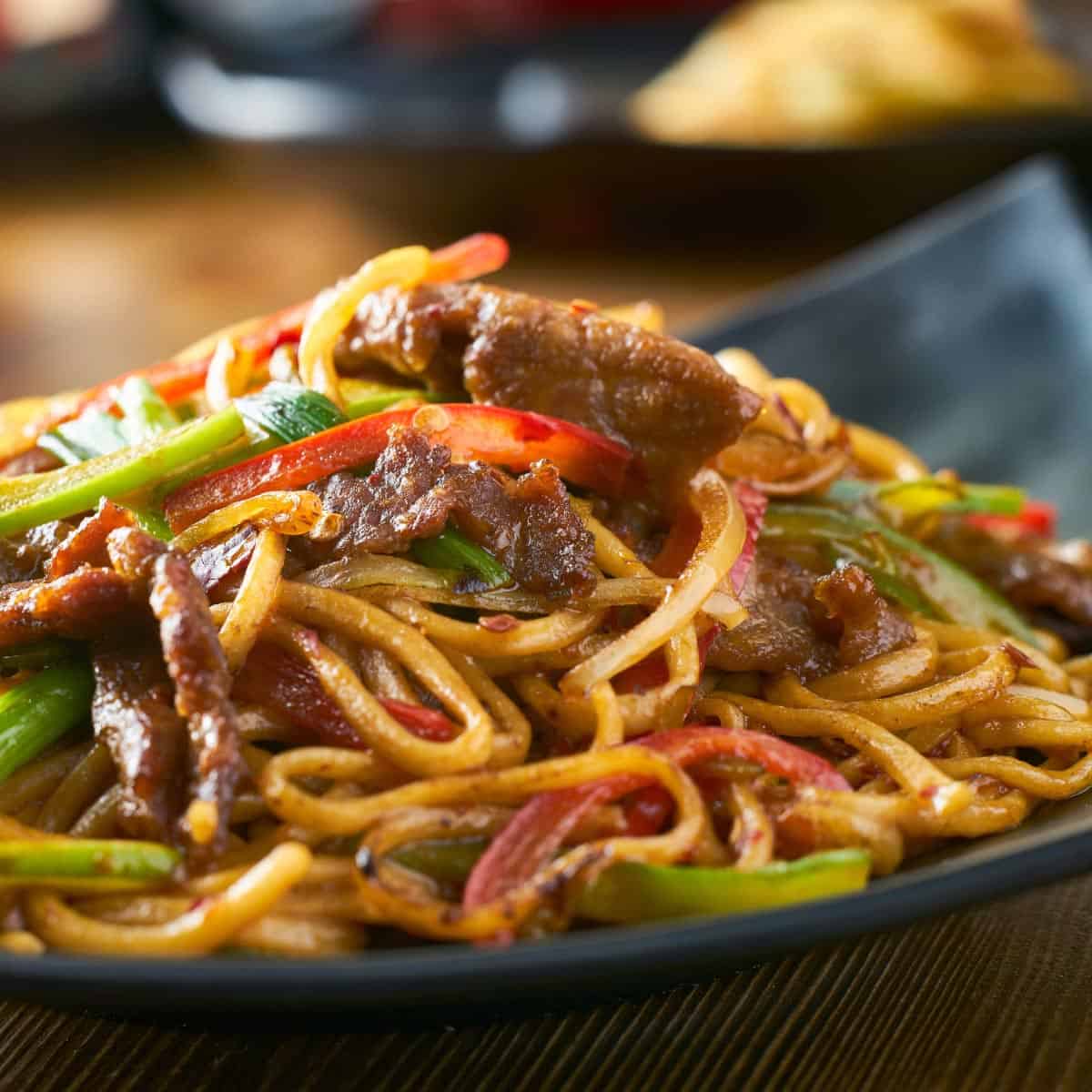 Lo mein with beef and bell peppers on a black plate.